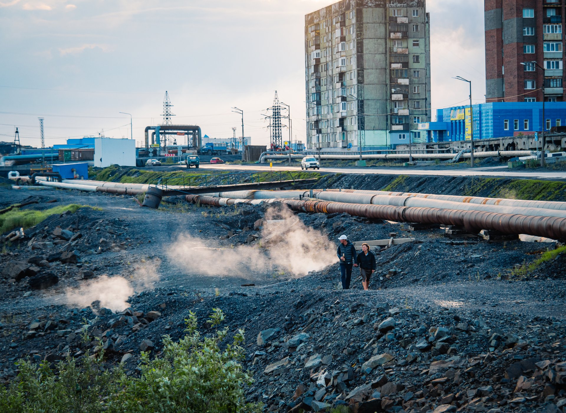 Residents of Norilsk are walking along an abandoned embankment near a lake with industrial water.