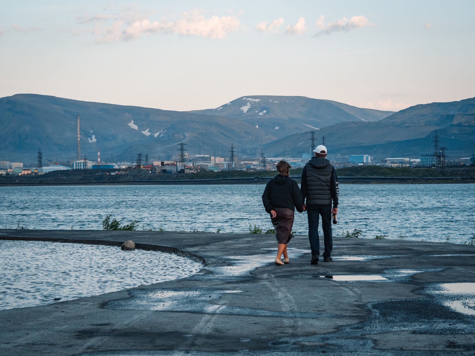 Residents of Norilsk are walking along an abandoned embankment near a lake with industrial water.